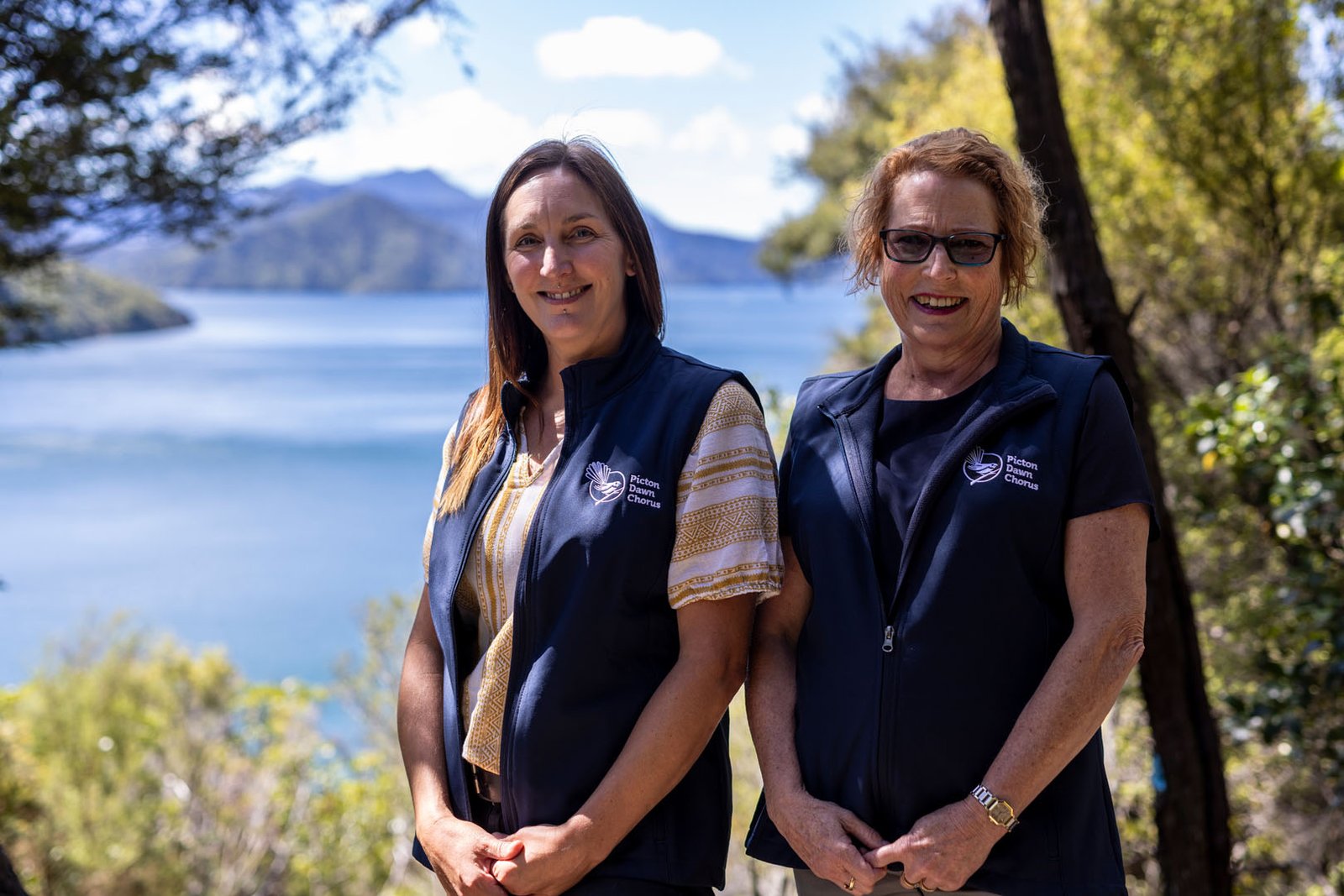 Two women standing infront of sea and mountains